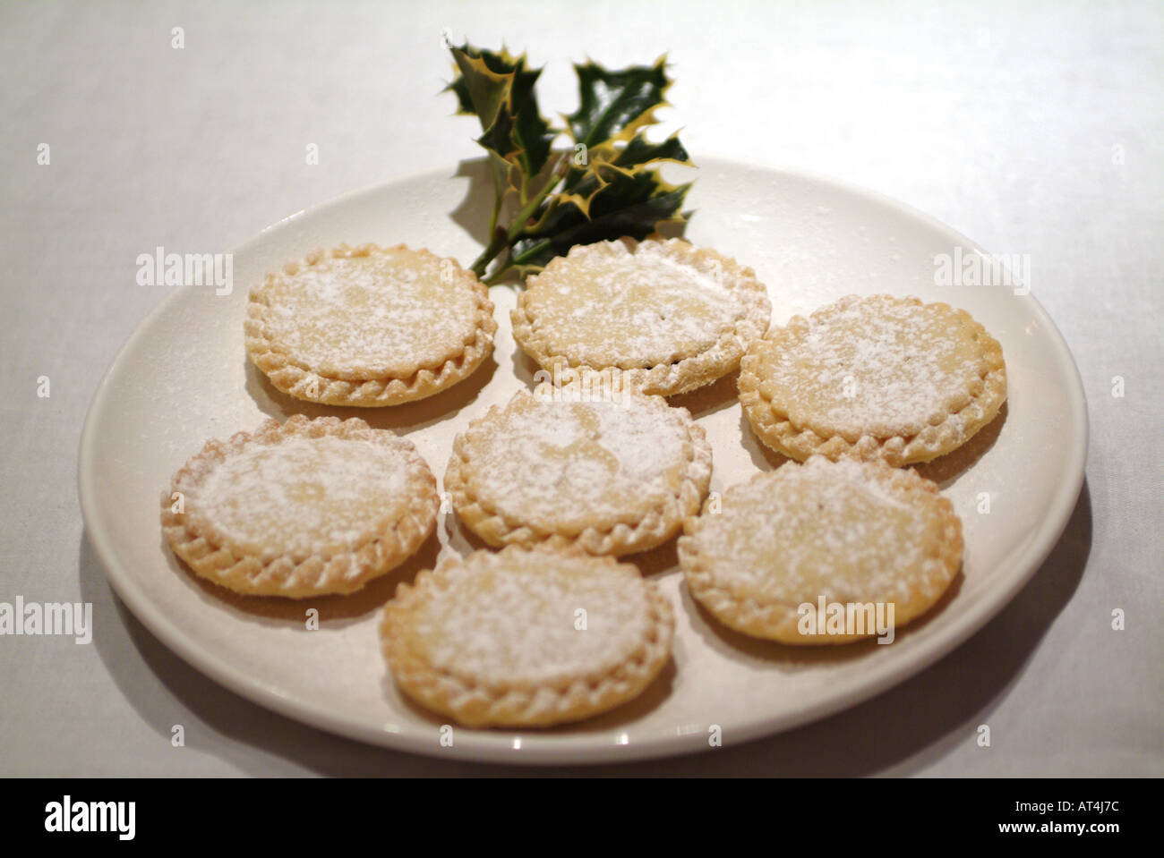 Mince Pies Sprinkled With Icing Sugar on White Plate With Sprig of Holly Stock Photo