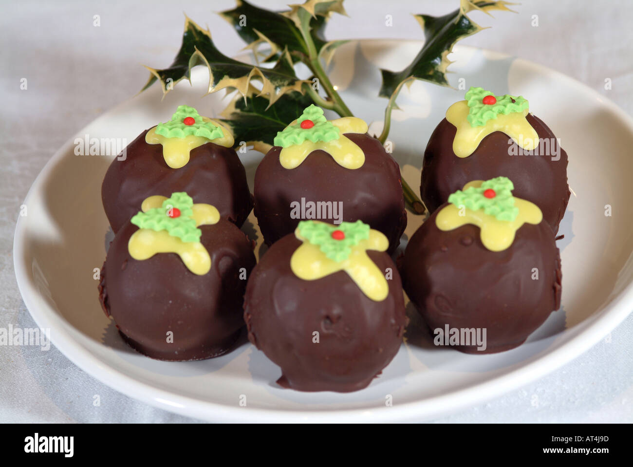 Chocolate Fancy Cakes Shaped Like Christmas Puddings on a White Plate with Holly Sprig Stock Photo