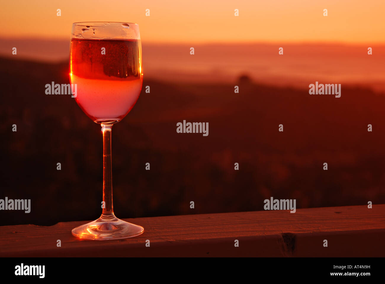 Glass of rose wine on wooden rail at sunset Stock Photo