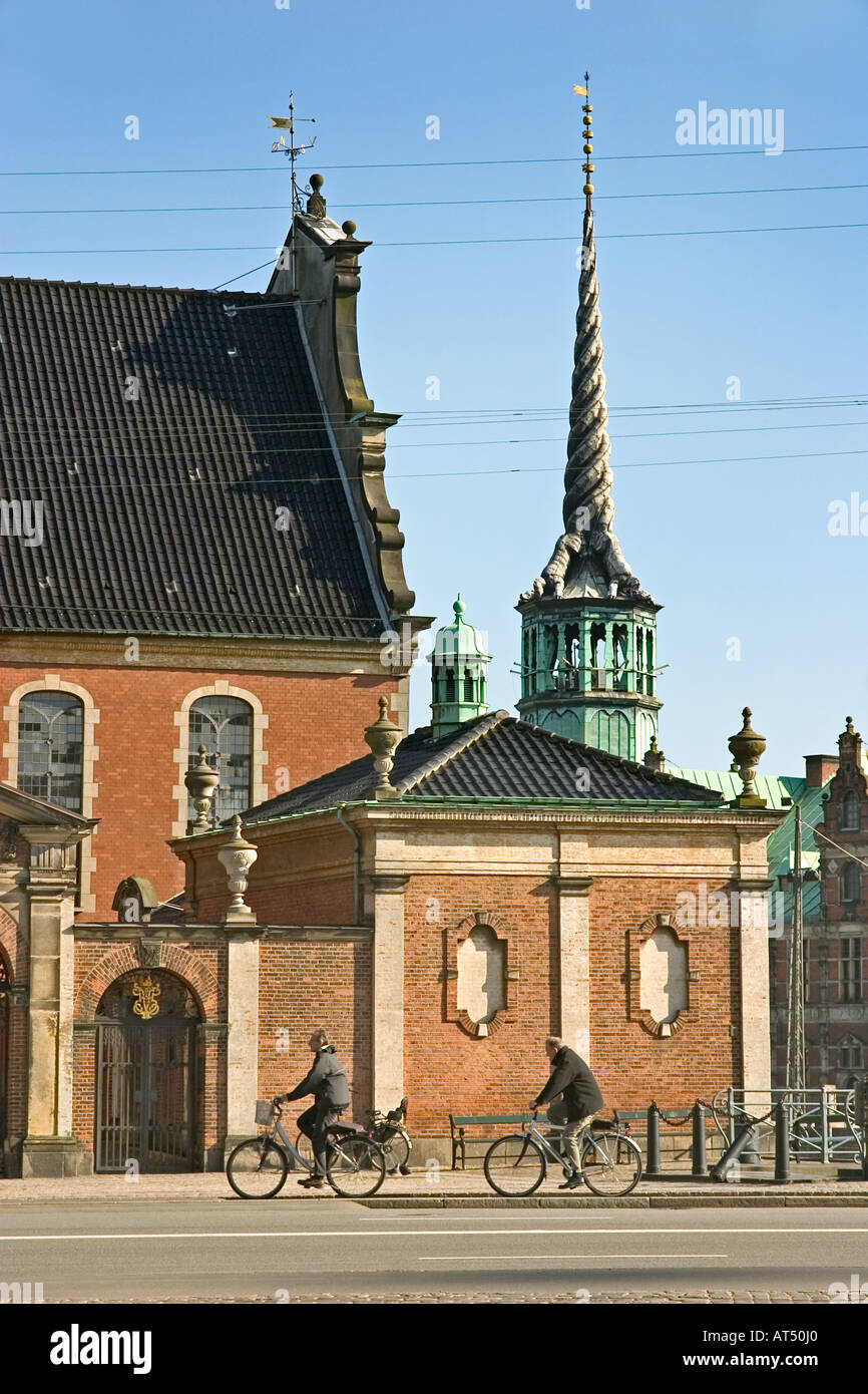 Two bikers passing Holmens Kirke Church with the sipre of the Børsen Stock Exchange in the background Copenhagen Denmark Stock Photo