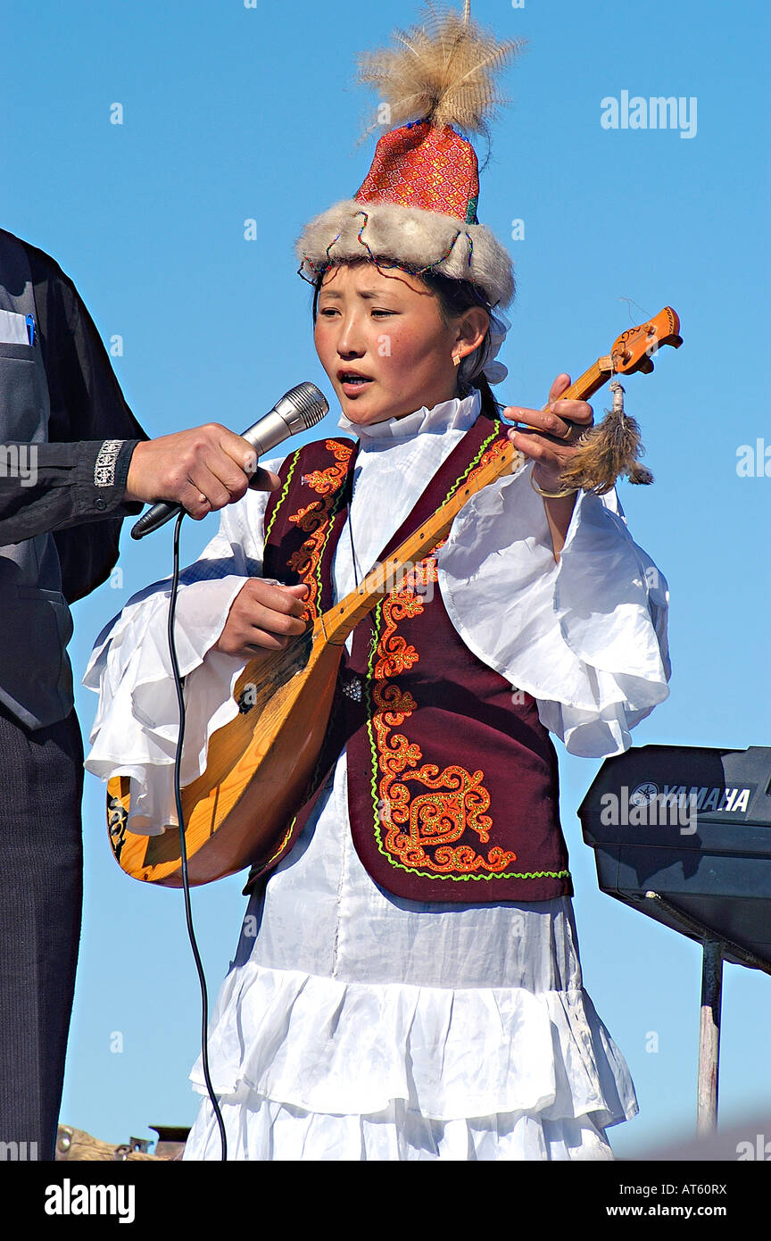A young kazakh girl in traditional dress sings and plays a dombro at the annual Eagle Hunting Festival, Sagsai, Mongolia Stock Photo