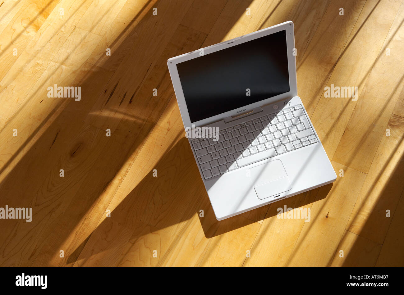Apple Ibook G4 laptop computer sitting on a real wooden floor in the afternoon sunshine Stock Photo