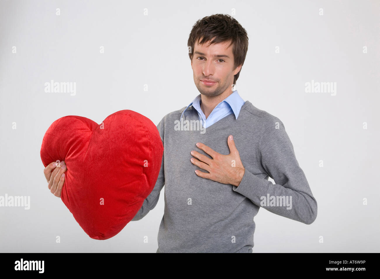 young-man-holding-heart-shaped-cushion-portrait-AT6W9P.jpg