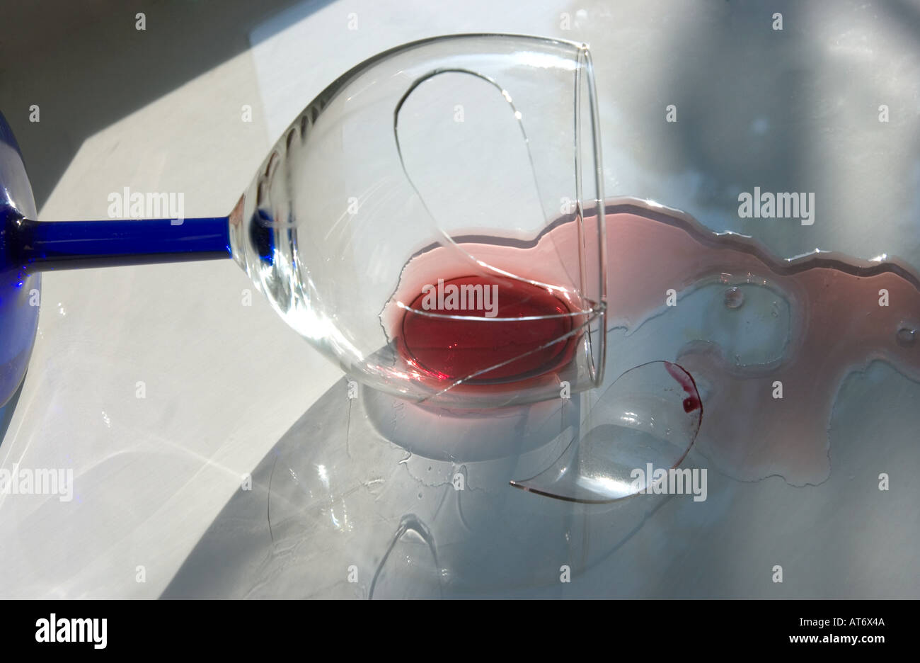 A blue stemmed wineglass broken and spilling the remains of a glass of red wine Stock Photo