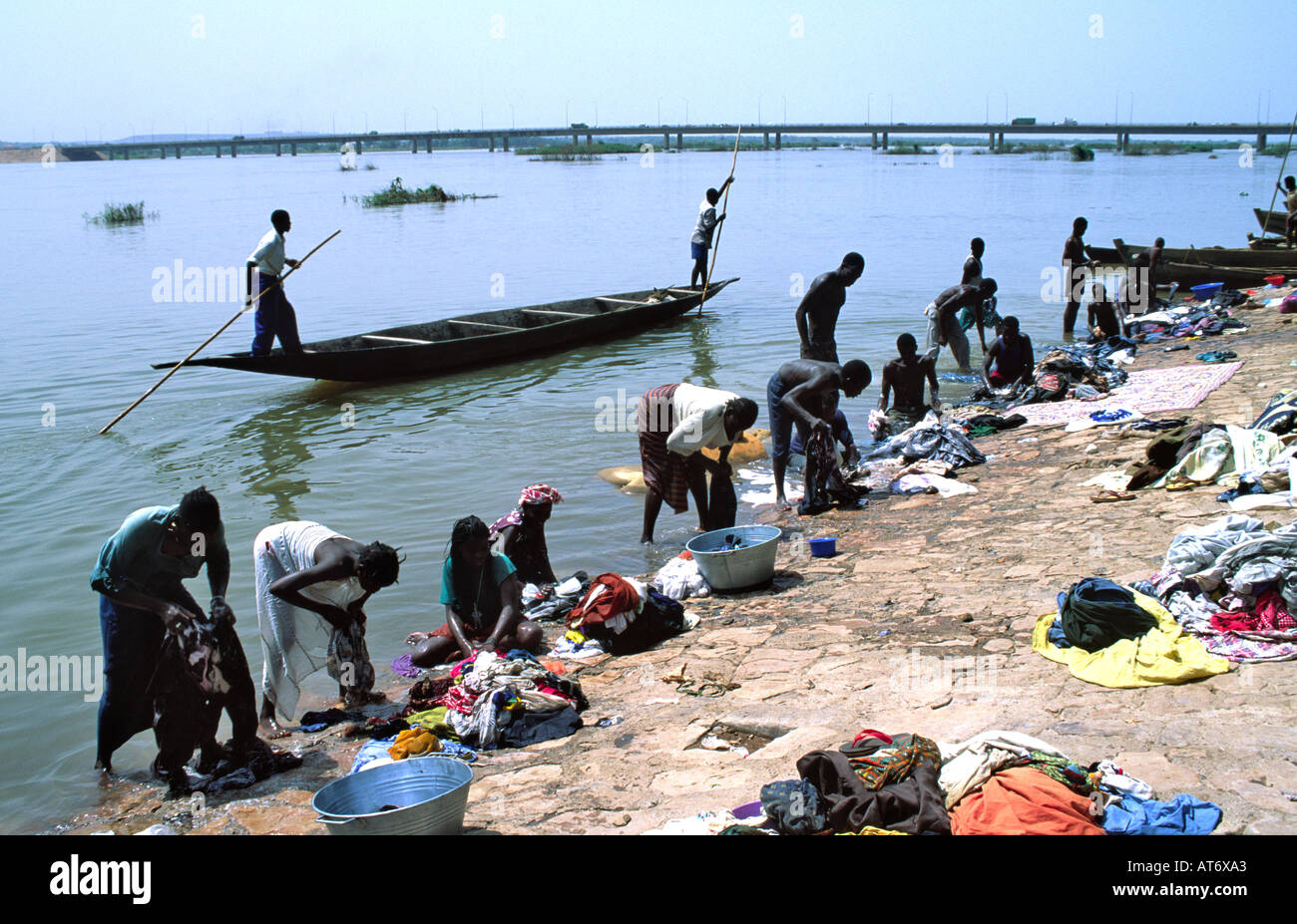 Men punting a pirogue with poles and men and women washing clothes on the banks of the River Niger in the capital city of Bamako. Mali Stock Photo