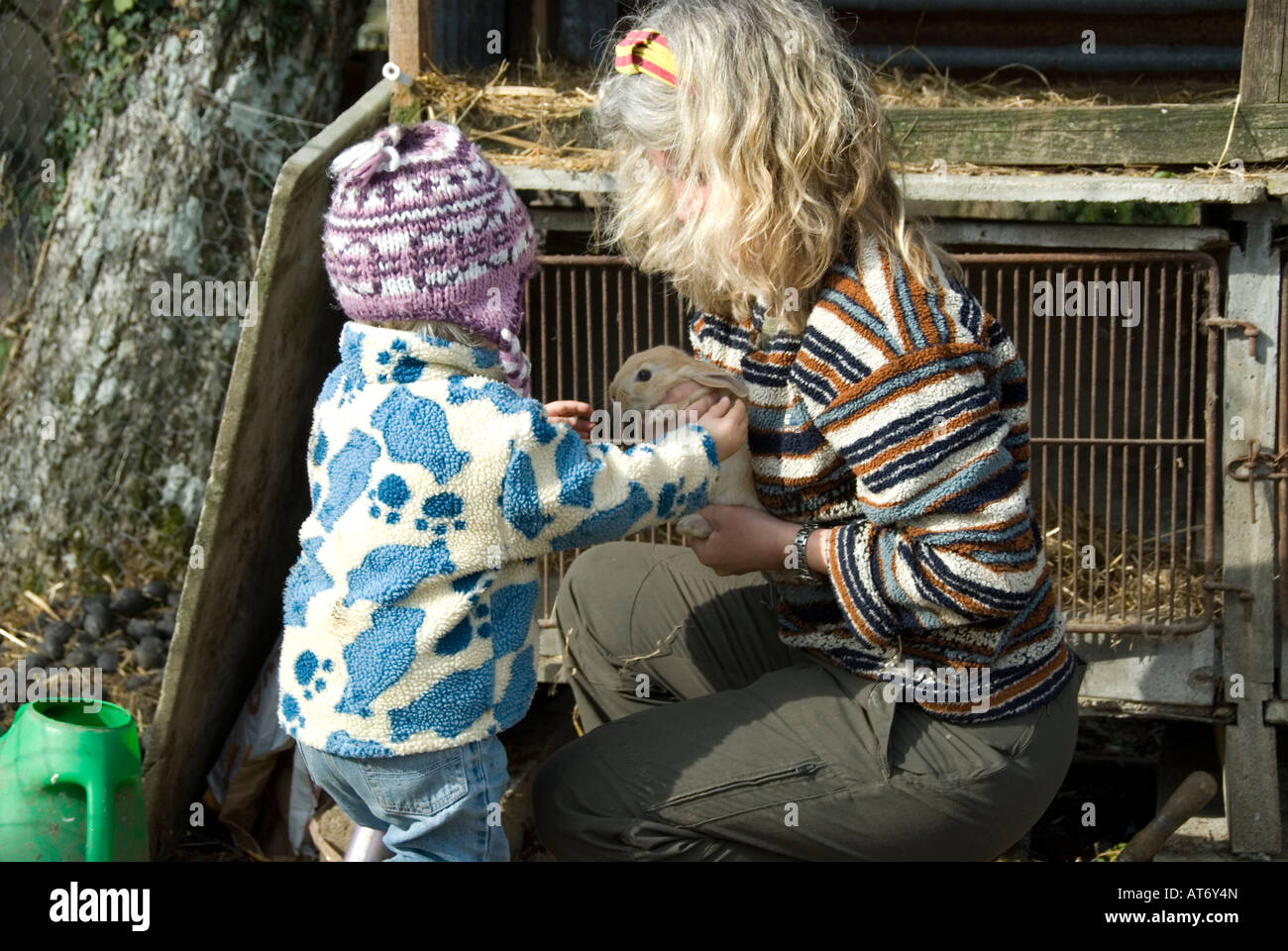 Mum and child cleaning out the rabbit hutch on their smallholding Stock