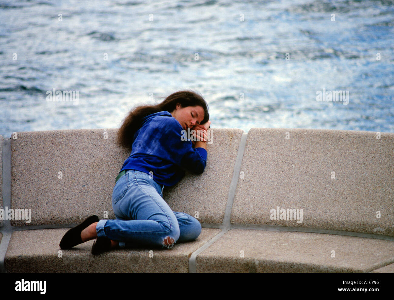 Young female sleeping on concrete seat at Sydney Opera House Australia