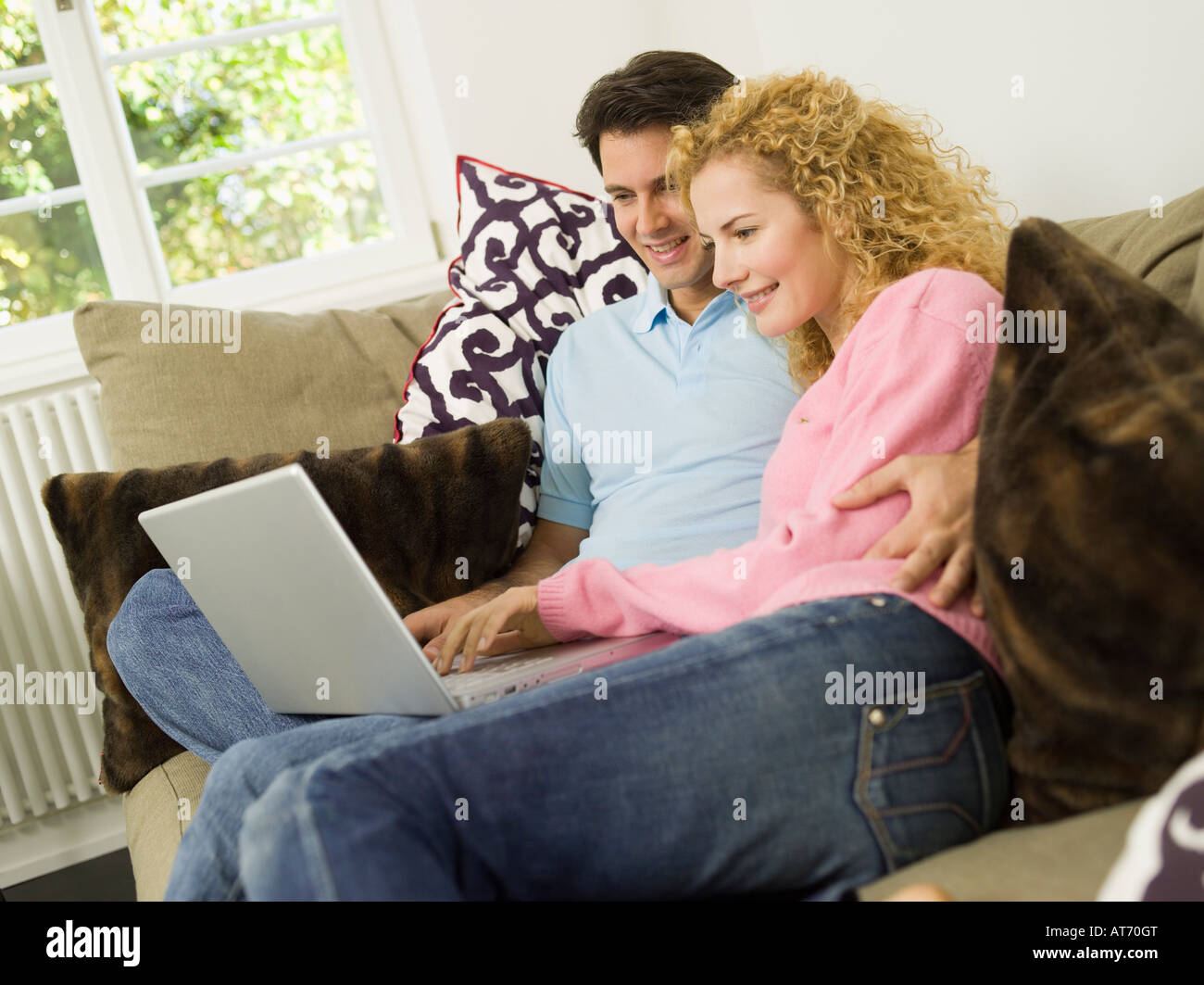 Young couple on sofa using laptop, smiling Stock Photo - Alamy