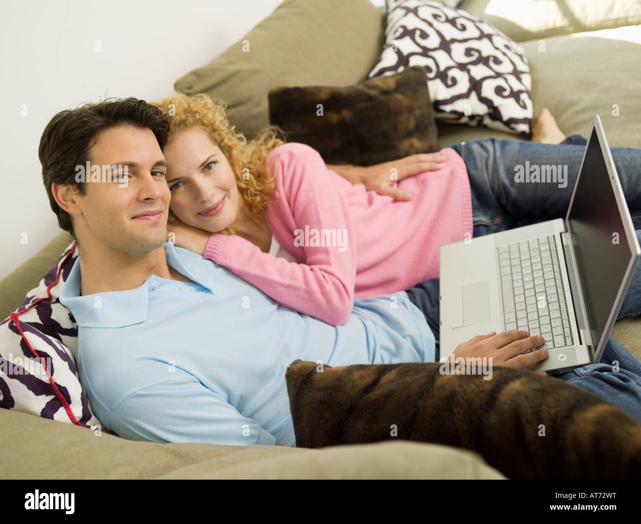 Young couple on sofa using laptop, smiling Stock Photo - Alamy