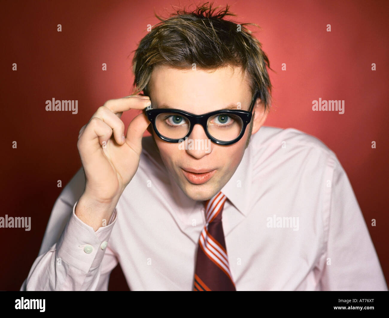 Young caucasian hipster business guy in pink shirt tying a striped tie in the studio. Stock Photo