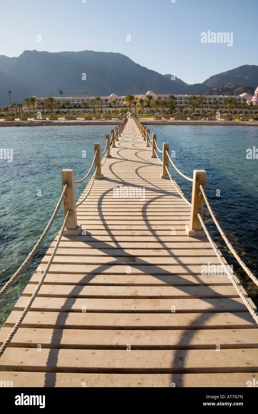 Taba Heights Sinai Egypt Wooden jetty in Red Sea with view back to beach and hotel in resort beyond in late afternoon sunshine Stock Photo