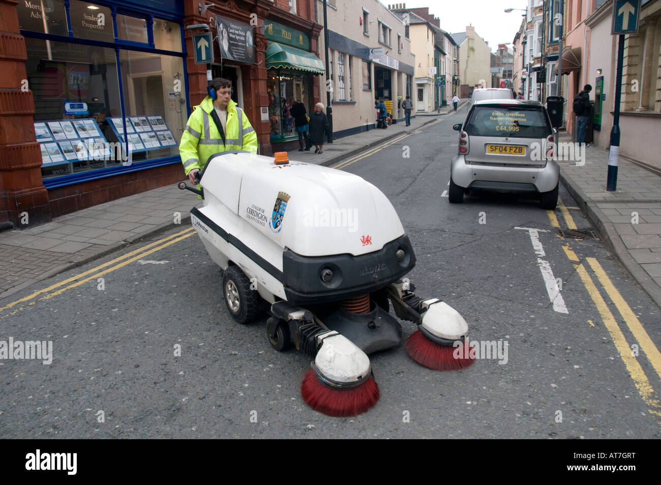 Council worker cleaning the streets of Aberystwyth using a noisy mechanical road sweeping vacuum cleaner wearing ear protection Stock Photo