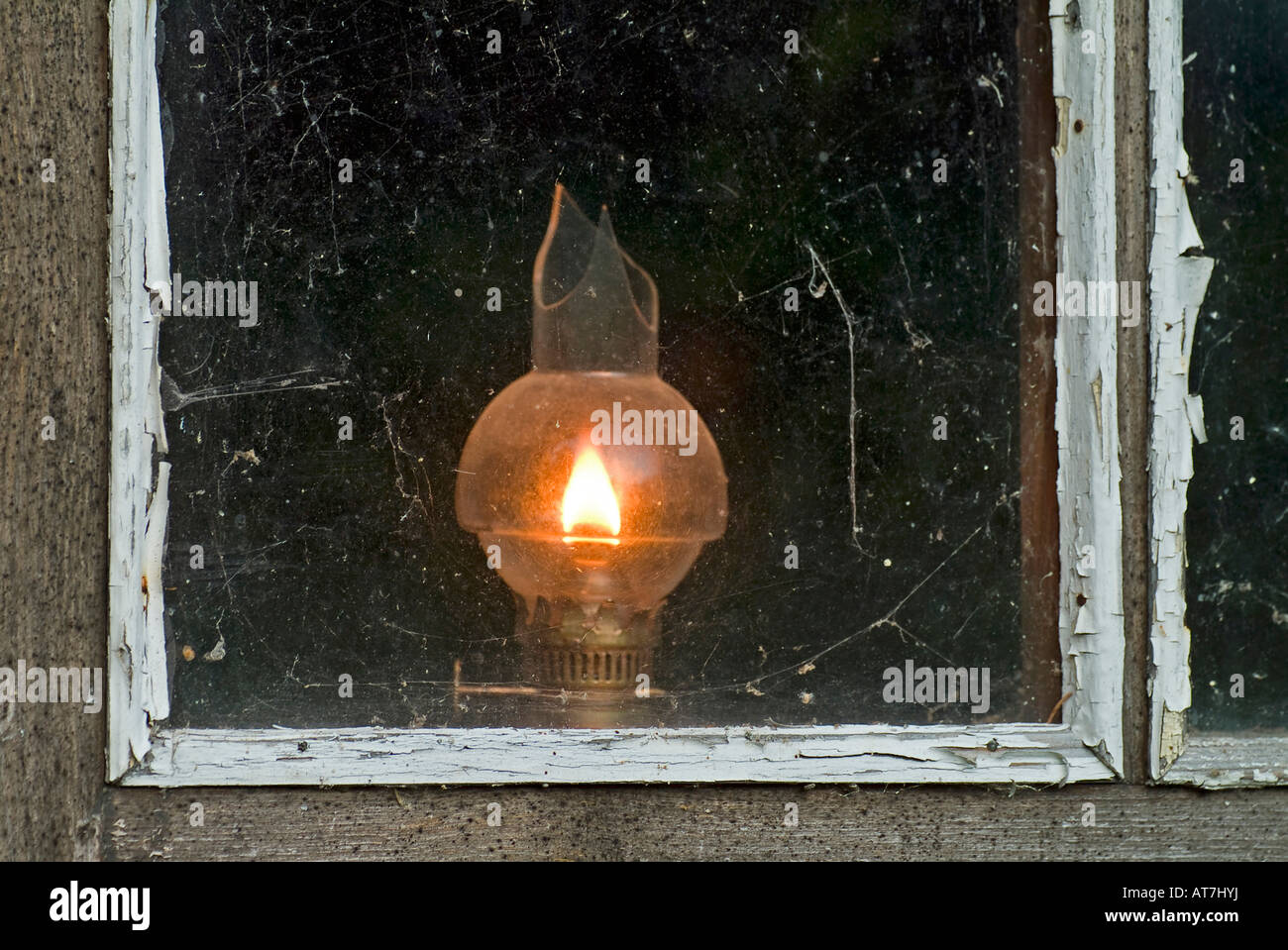 old oil lamp with broken glass burning at window of a timber wooden