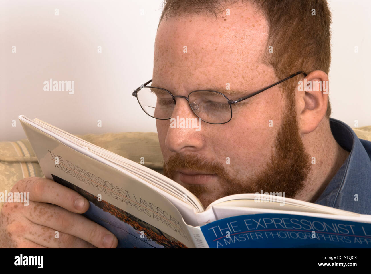 young man with poor eyesight wearing glasses straining eyes to read book, incorrect spectacles, too close to book Stock Photo