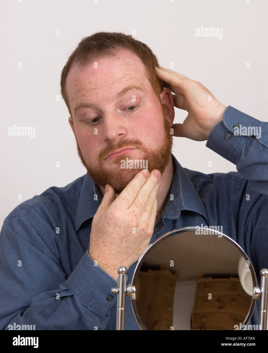 young man looking into small mirror admiring or questioning his grooming appearance does he like or is he proud of his beard, vanity, ginger hair Stock Photo