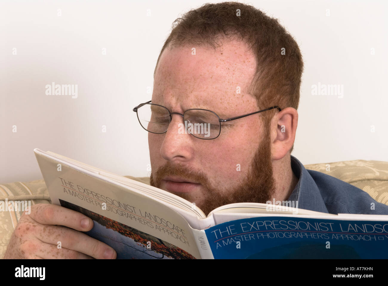 young man with poor eyesight wearing glasses straining eyes to read book Stock Photo
