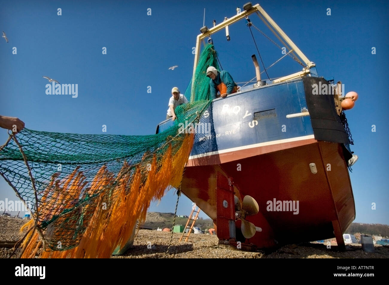 Two crewmen from the small fishing boat Roys Boys check the fishing nets after being winched up Hastings beach Stock Photo