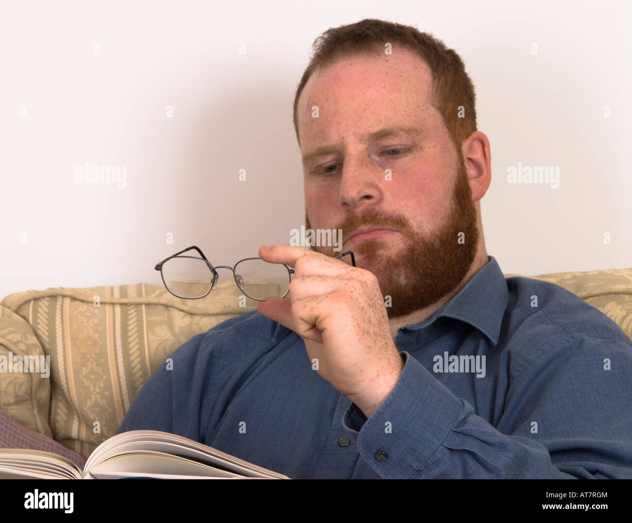 young man with poor eyesight wearing glasses straining eyes to read book Stock Photo