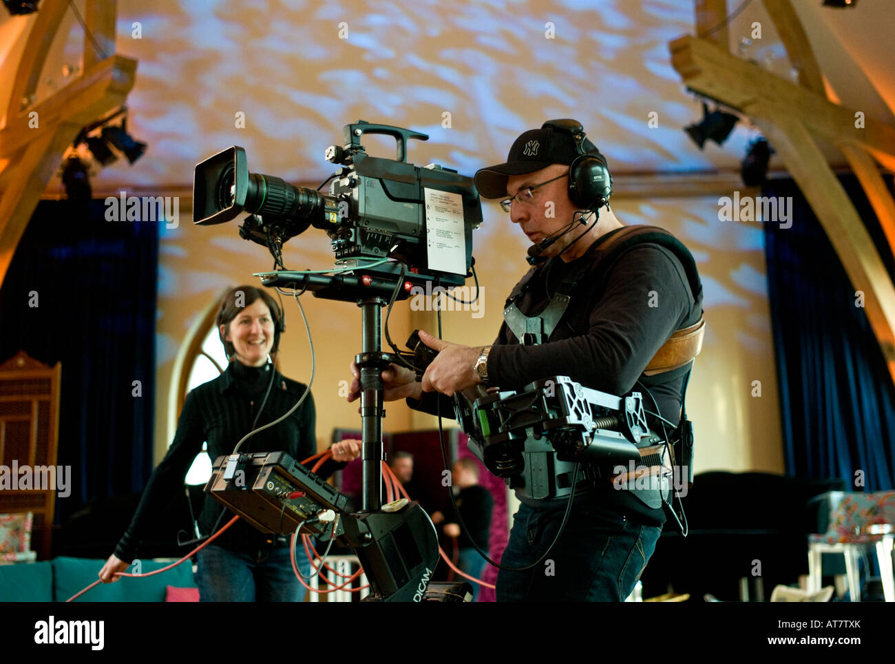A S4C Cameraman operating steadicam steadycam broadcast video camera in television studio with female cable basher assistant UK Stock Photo