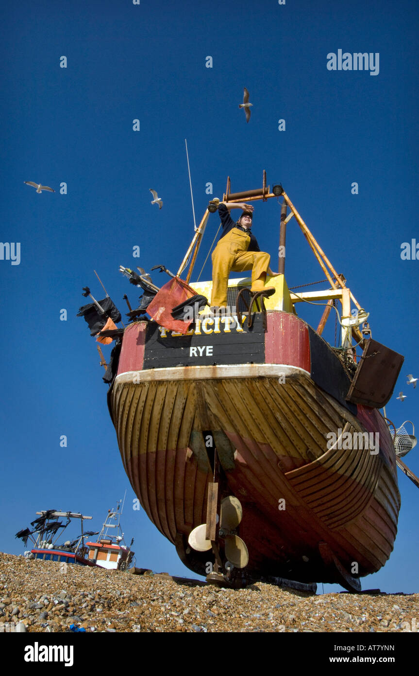 A crewman in oilskins on a small wooden fishing boat ashore on the beach at Hastings Sussex Stock Photo