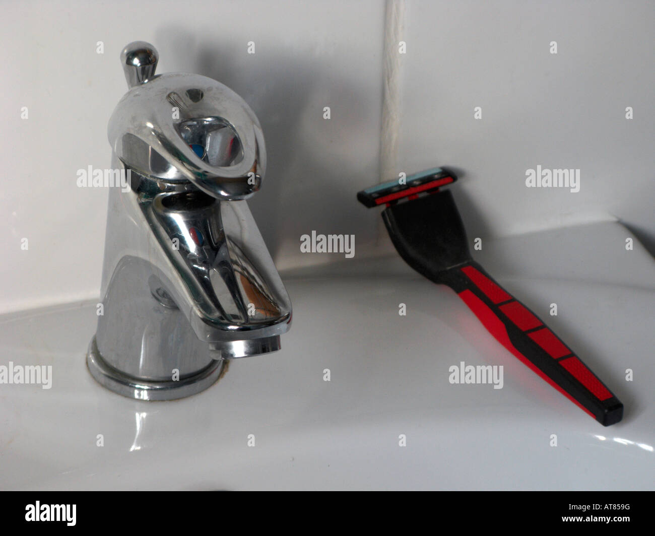 modern single bathroom mixer tap with white sink white tiles and mans razor Belfast Stock Photo
