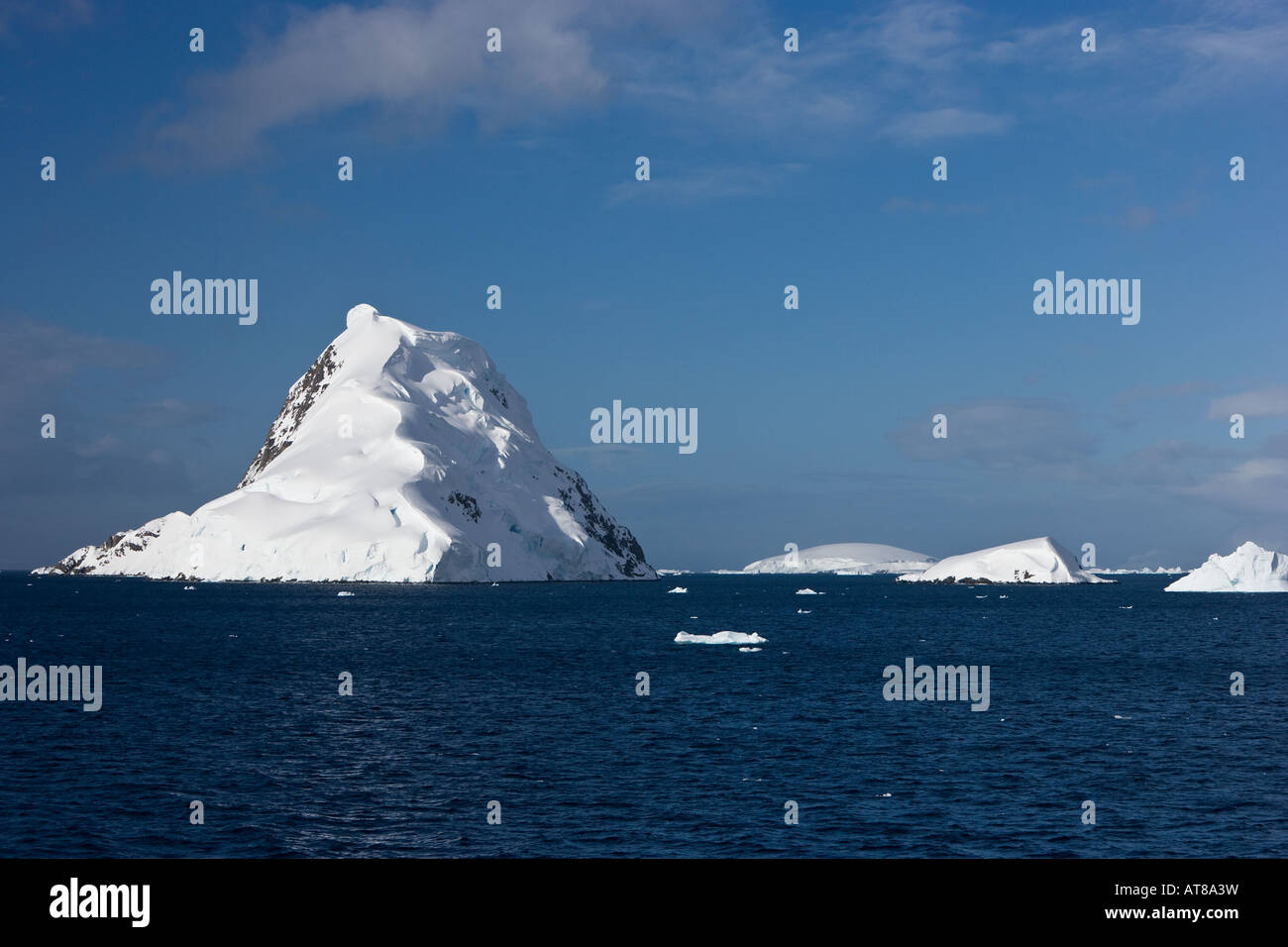 Snow capped islands of the Antarctic peninsula surrounded by icebergs and sea against a blue sky background Stock Photo