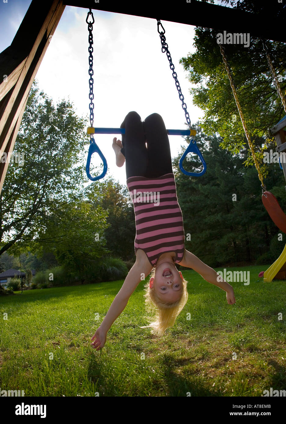 Child swinging upside down on a backyard swing Stock Photo