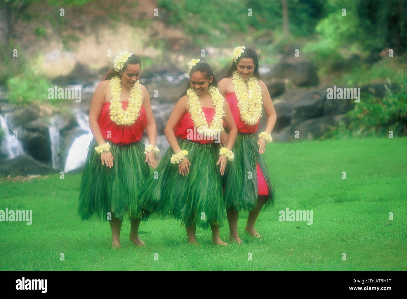 Three Hula Dancers near Waterfall in ti leaf skirts and yellow plumeria