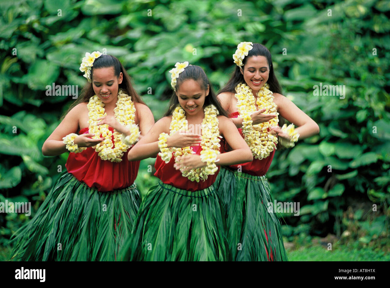 Three Hula Dancers in ti leaf skirts and yellow plumeria leis