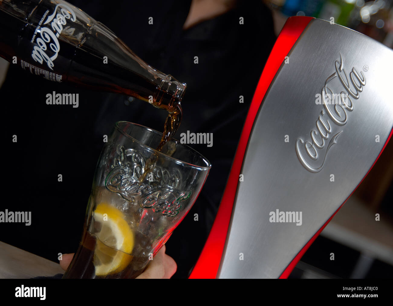 barperson pouring a traditional coke into a glass with ice and la slice of lemon Stock Photo