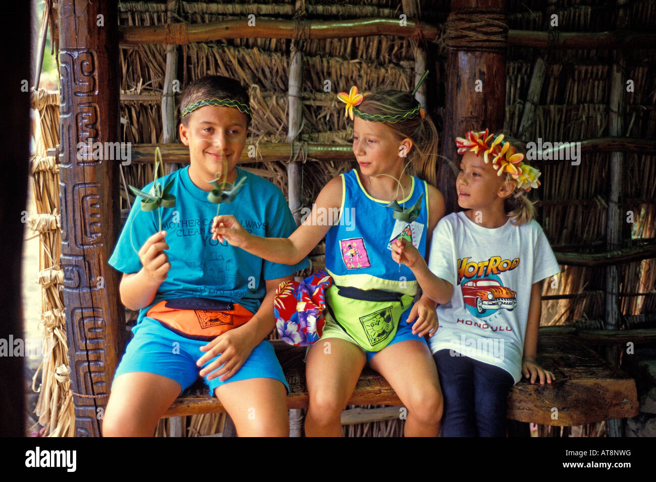 3 children smile modelling handmade lauhala woven headbands & hold their small crafts at the Polynesian Cultural Center, Oahu Stock Photo