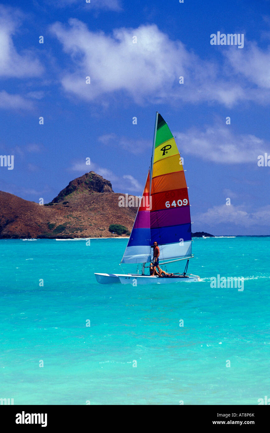 Catamaran, vivid rainbow striped sail glides in front of Moku lua