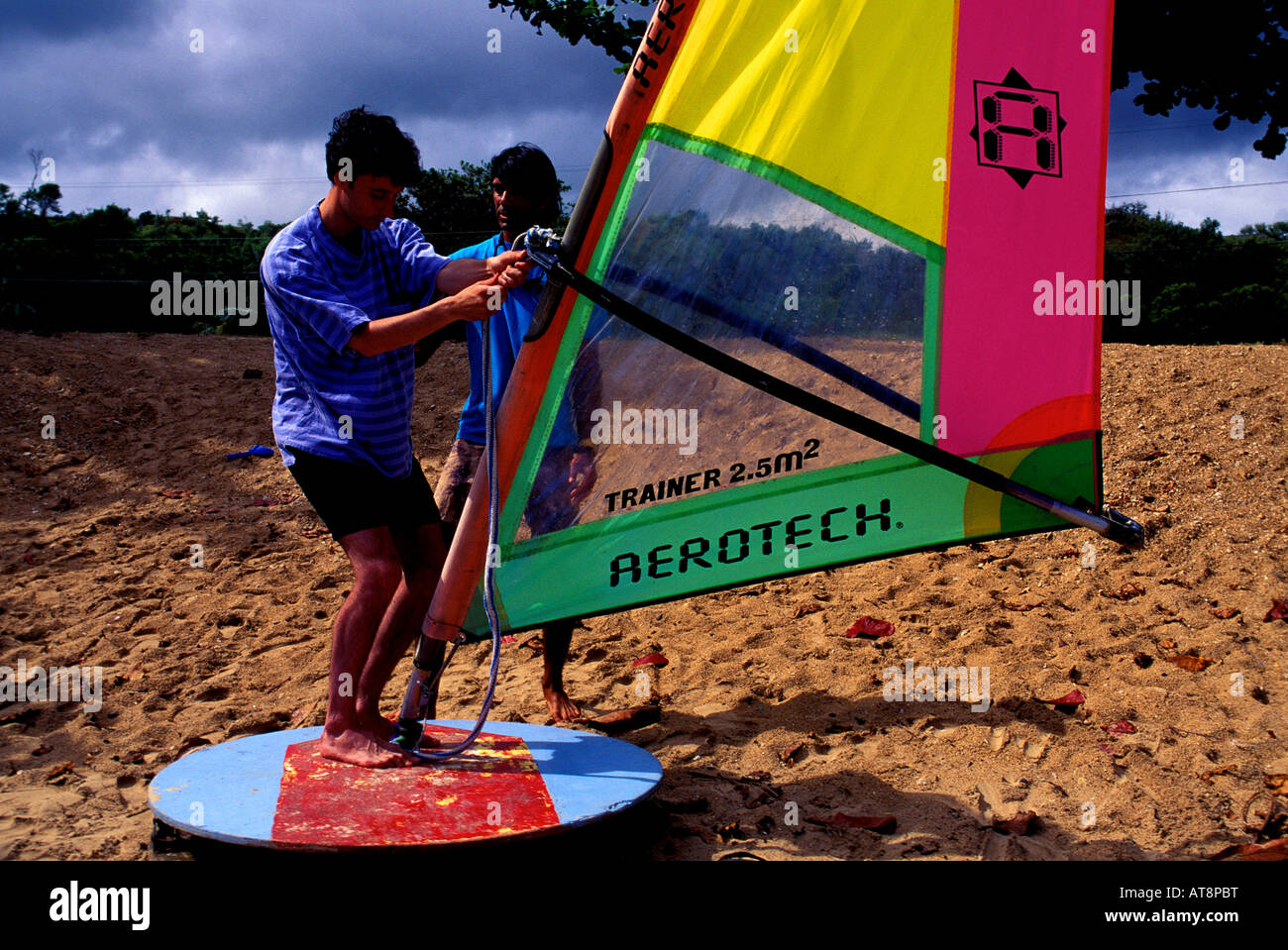 A man learns the technique of windsurfing on the sand of Anini Beach by