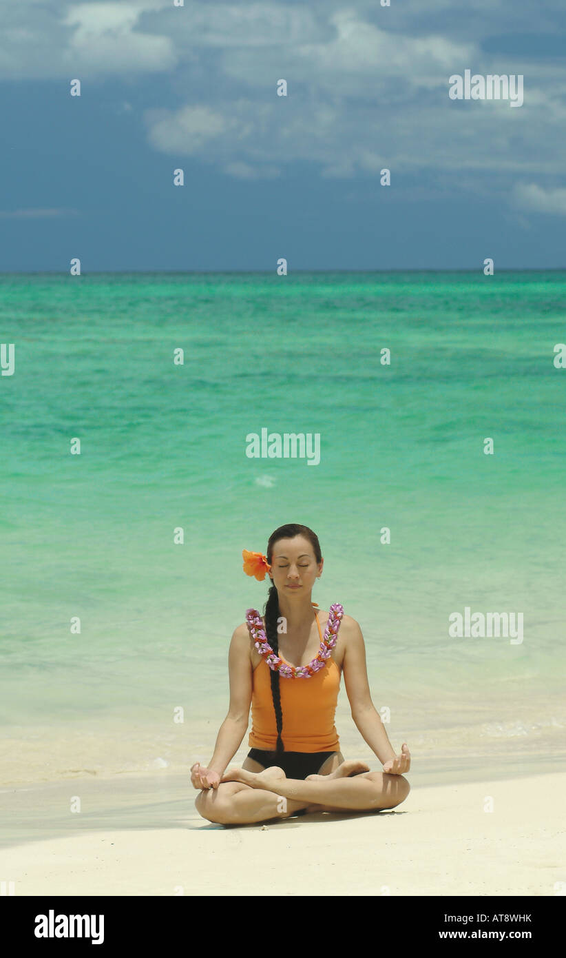 Woman meditating in lotus position wearing flower lei on white sand beach in Hawaii Stock Photo
