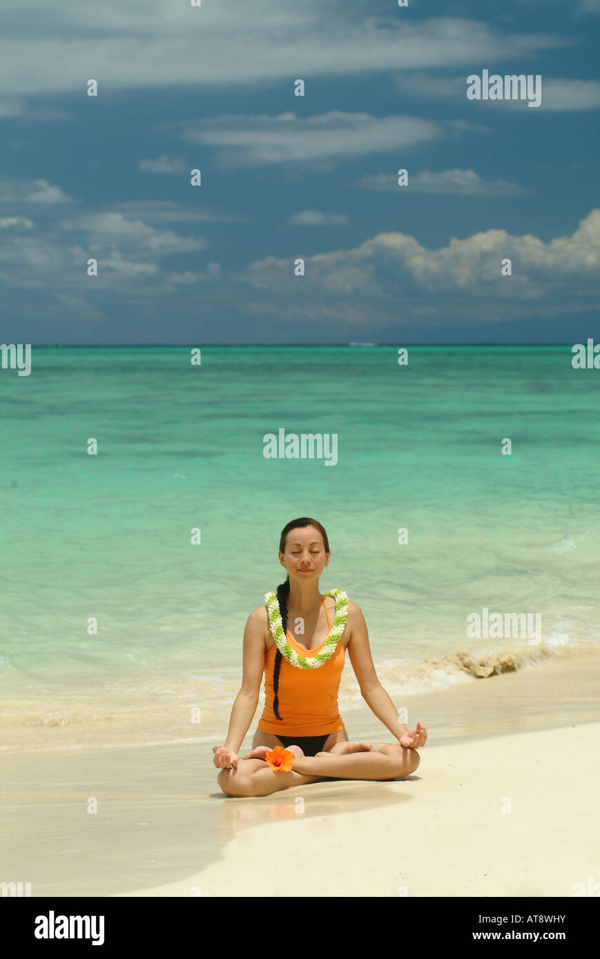 Woman meditating in lotus position wearing flower lei on white sand beach in Hawaii Stock Photo