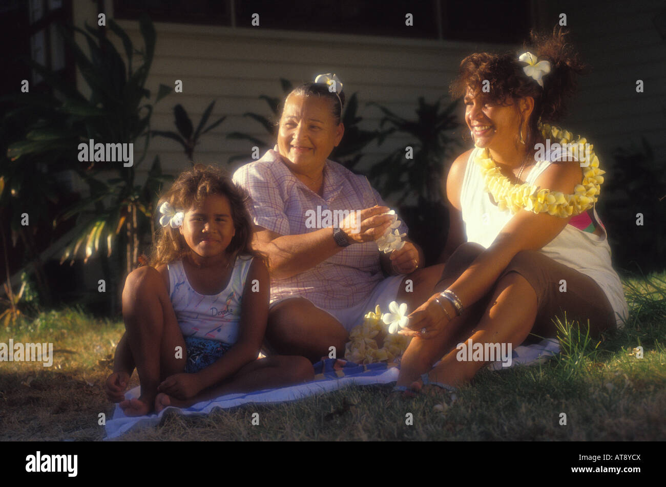 Local polynesian family relaxing out on the lawn in the sun and wearing leis Stock Photo