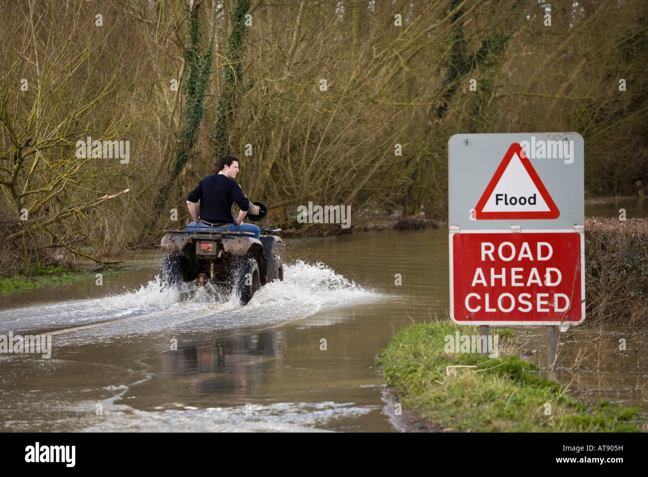 Two lads on a quad bike tackling the B4213 while it was closed due to flooding near Apperley, Gloucestershire in March 2007 Stock Photo