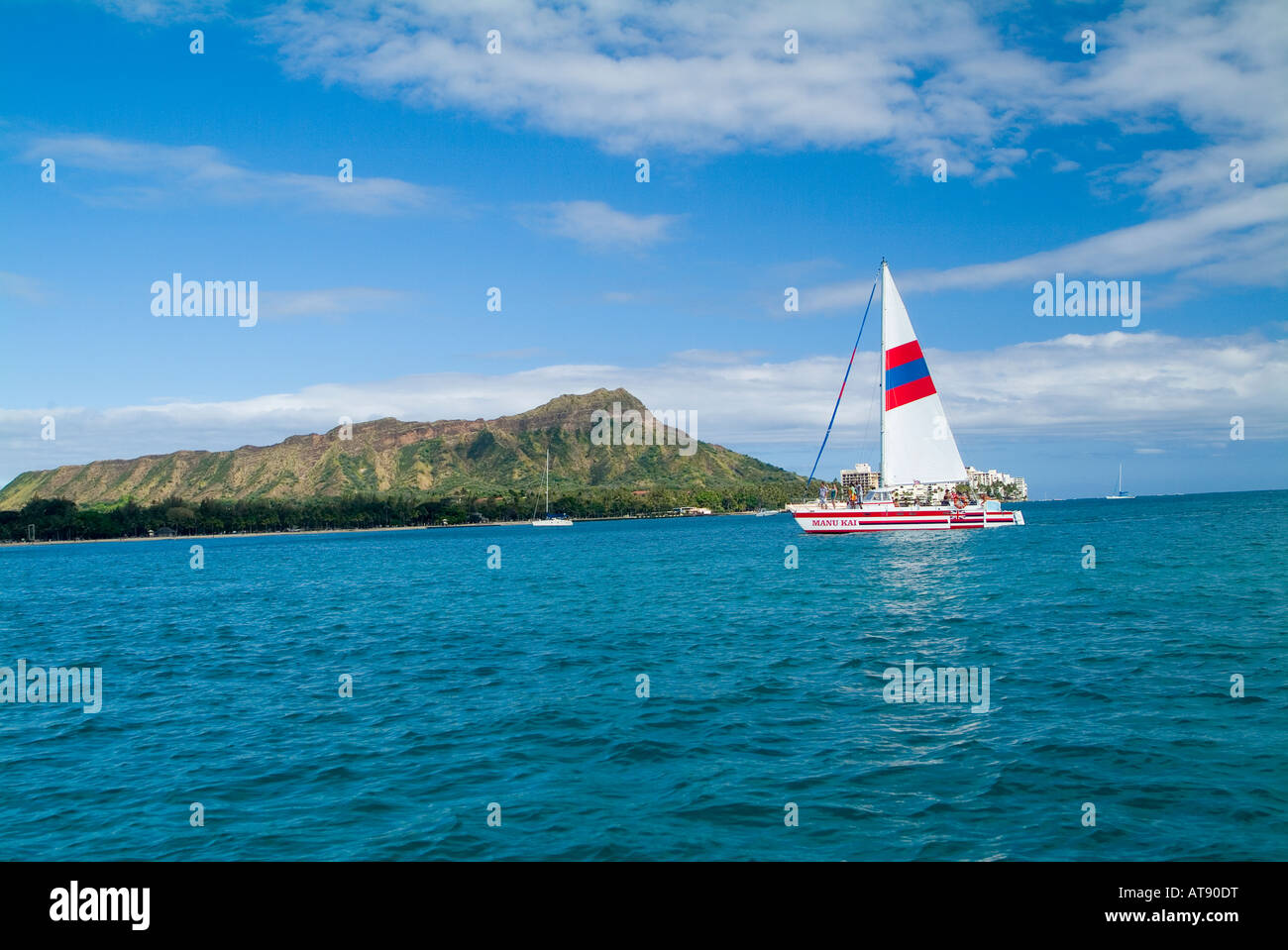 Long shot of Diamond Head from a sailboat off Waikiki with a catamaran sporting a white striped sail in the foreground. Stock Photo