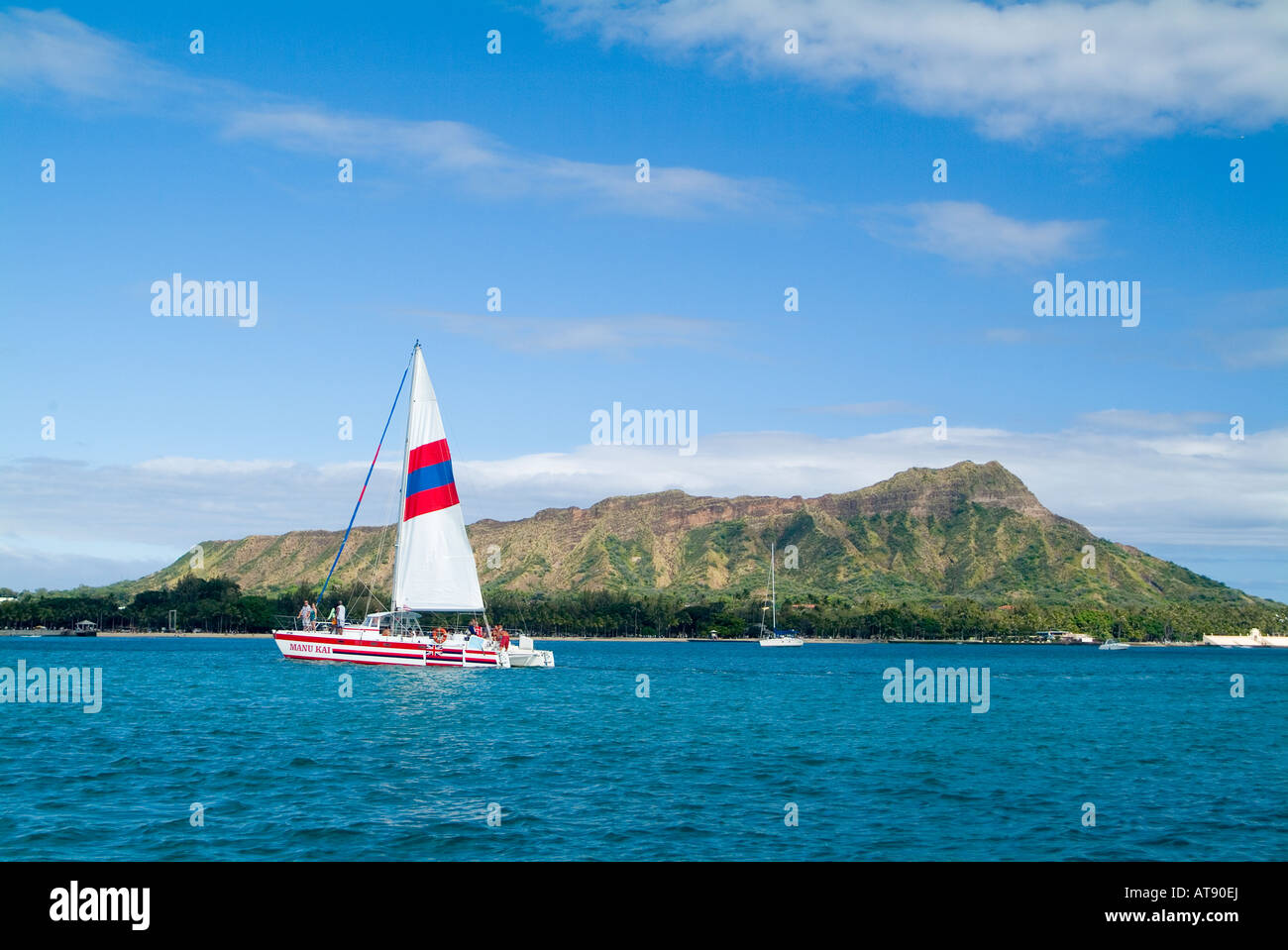 A catamaran cuts a path on the clear blue water in front of Diamond Head, Stock Photo
