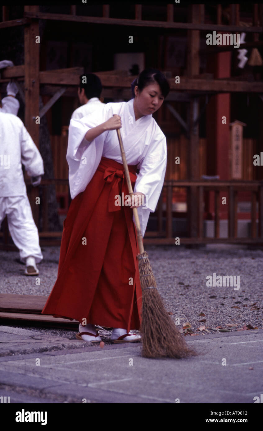 a japanese miko sweeping the inner grounds of a shinto shrine in