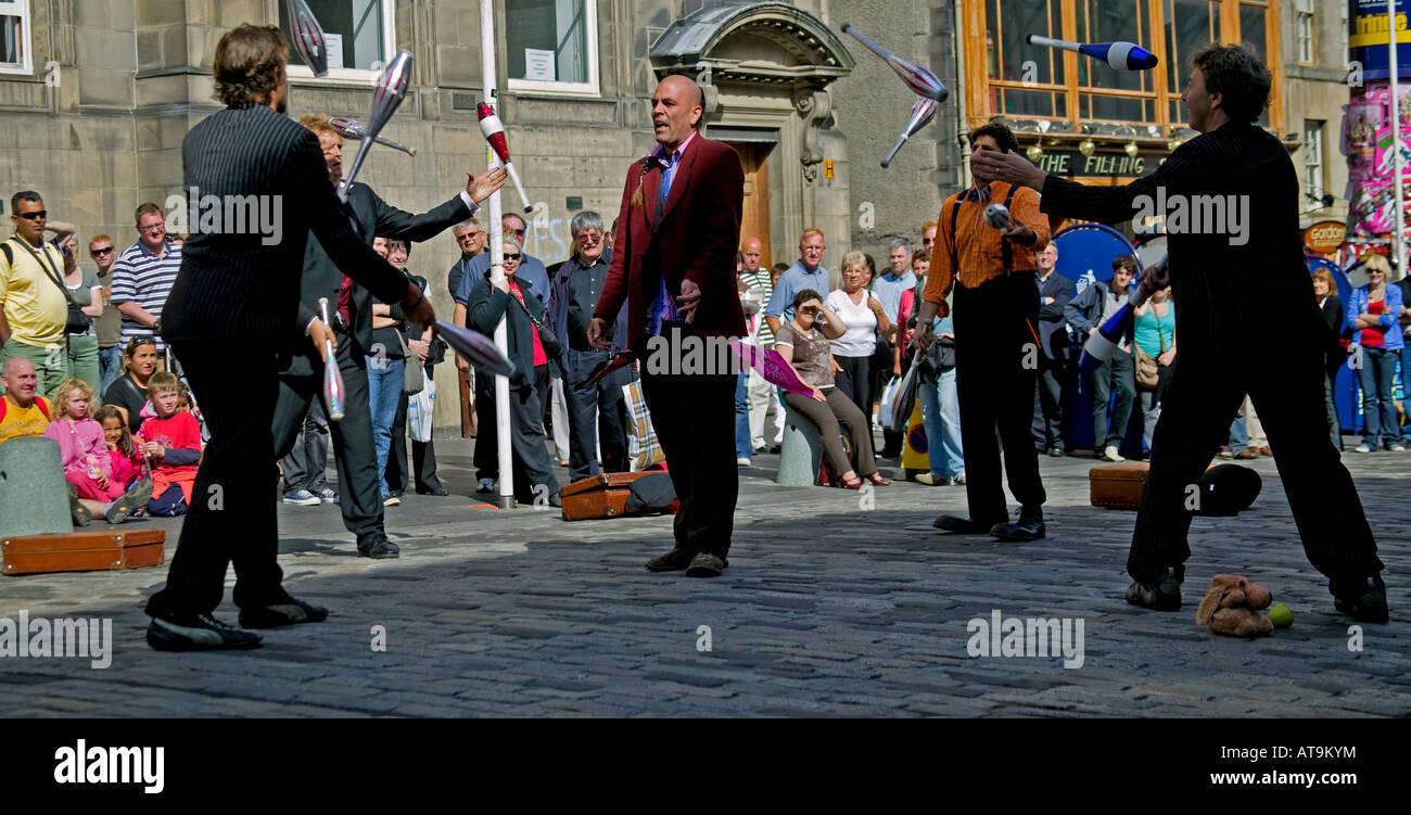 Street Performers throw juggle clubs past a colleagues head while he stands in the middle  Edinburgh Fringe Festival, Scotland Stock Photo