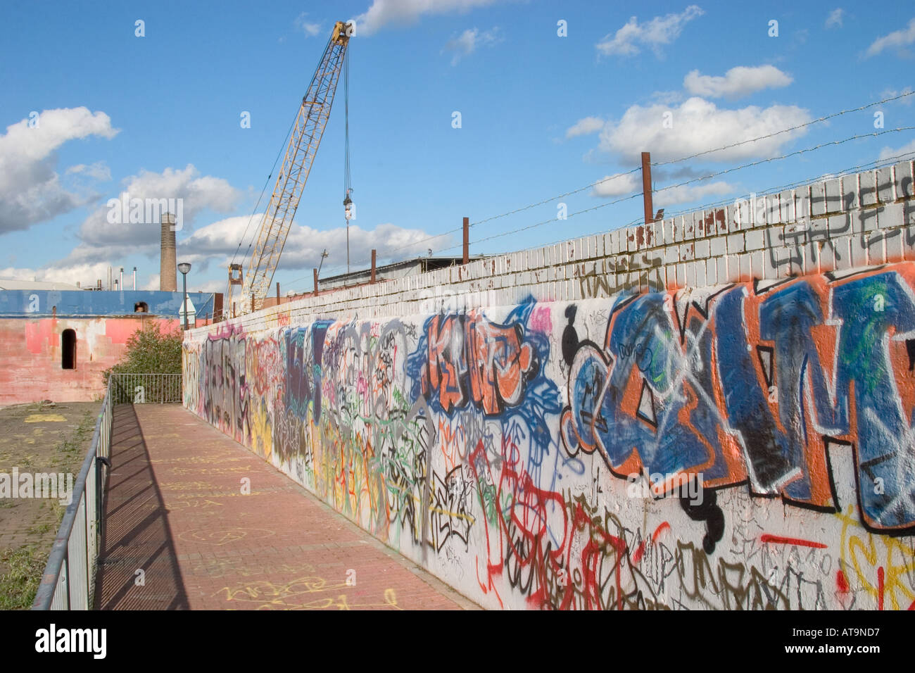 Industrial waterfront with colourful graffiti barbed wire and crane. Thames Path, North Greenwich, London, England Stock Photo