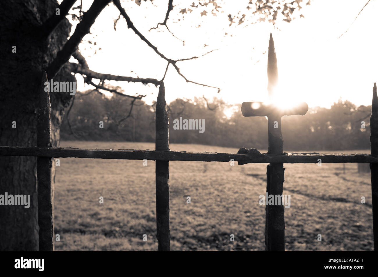 Moody conceptual image showing iron cross on fence with sunrise and field in the background Stock Photo