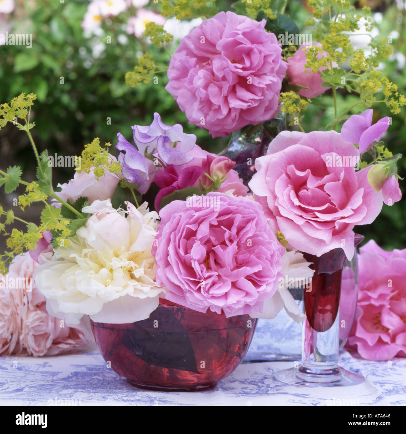 A floral still life with roses paeonies and sweet peas and cranberry glass in an English Garden Stock Photo