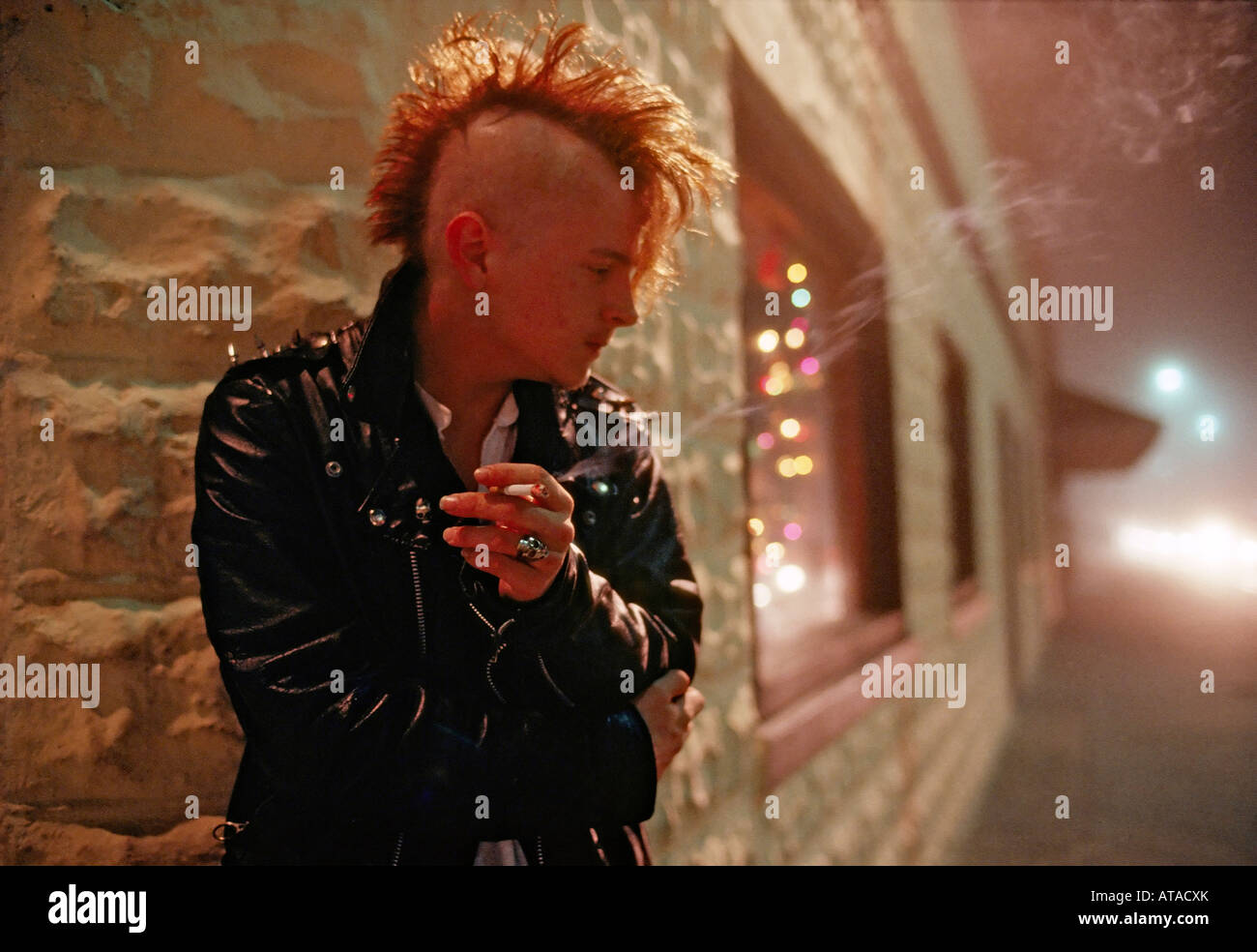 Young man with mohawk haircut smokes a cigarette outside an alternative nightclub club in Jacksonville Florida USA Stock Photo