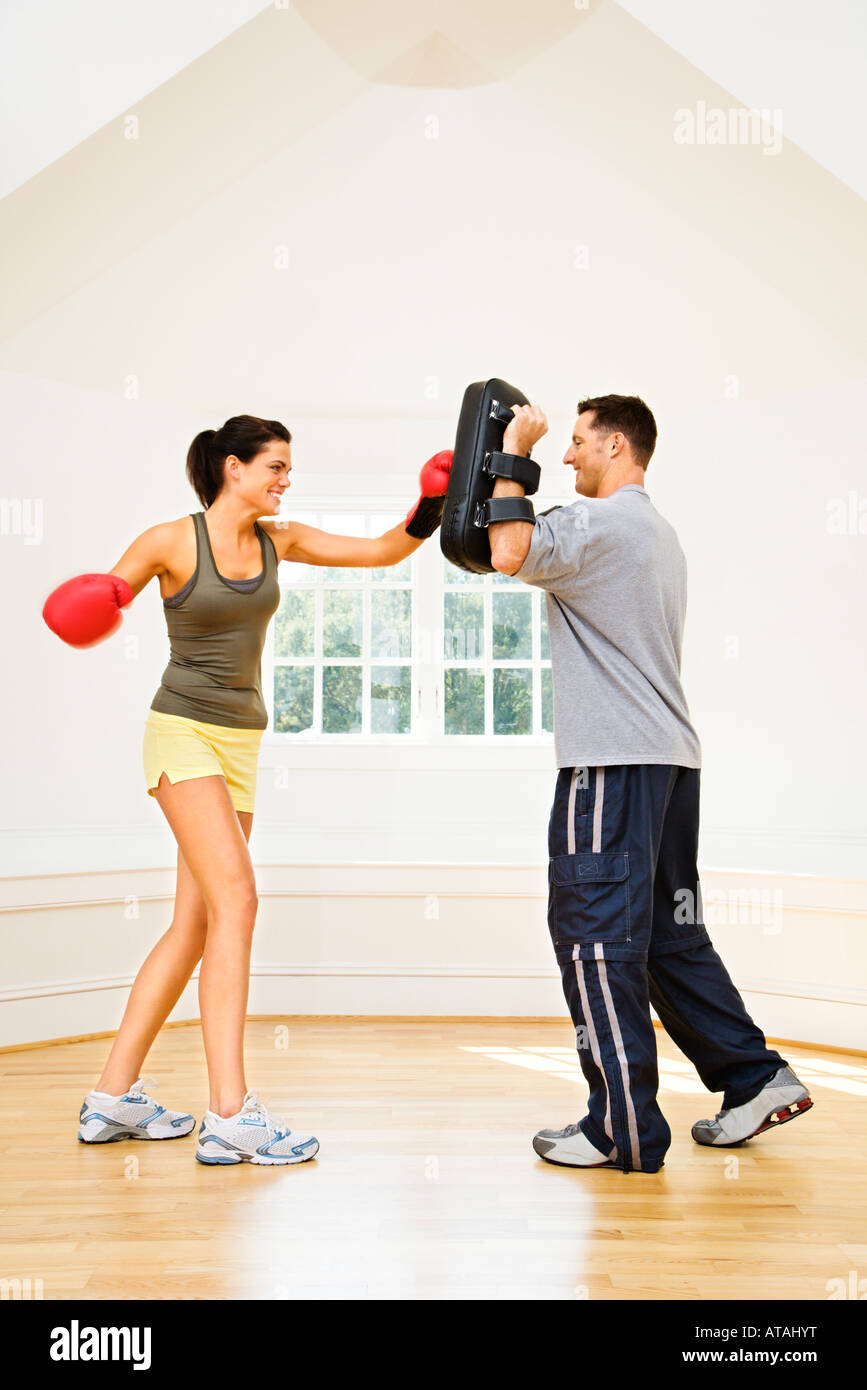 Woman wearing boxing gloves hitting training mits man is holding Stock