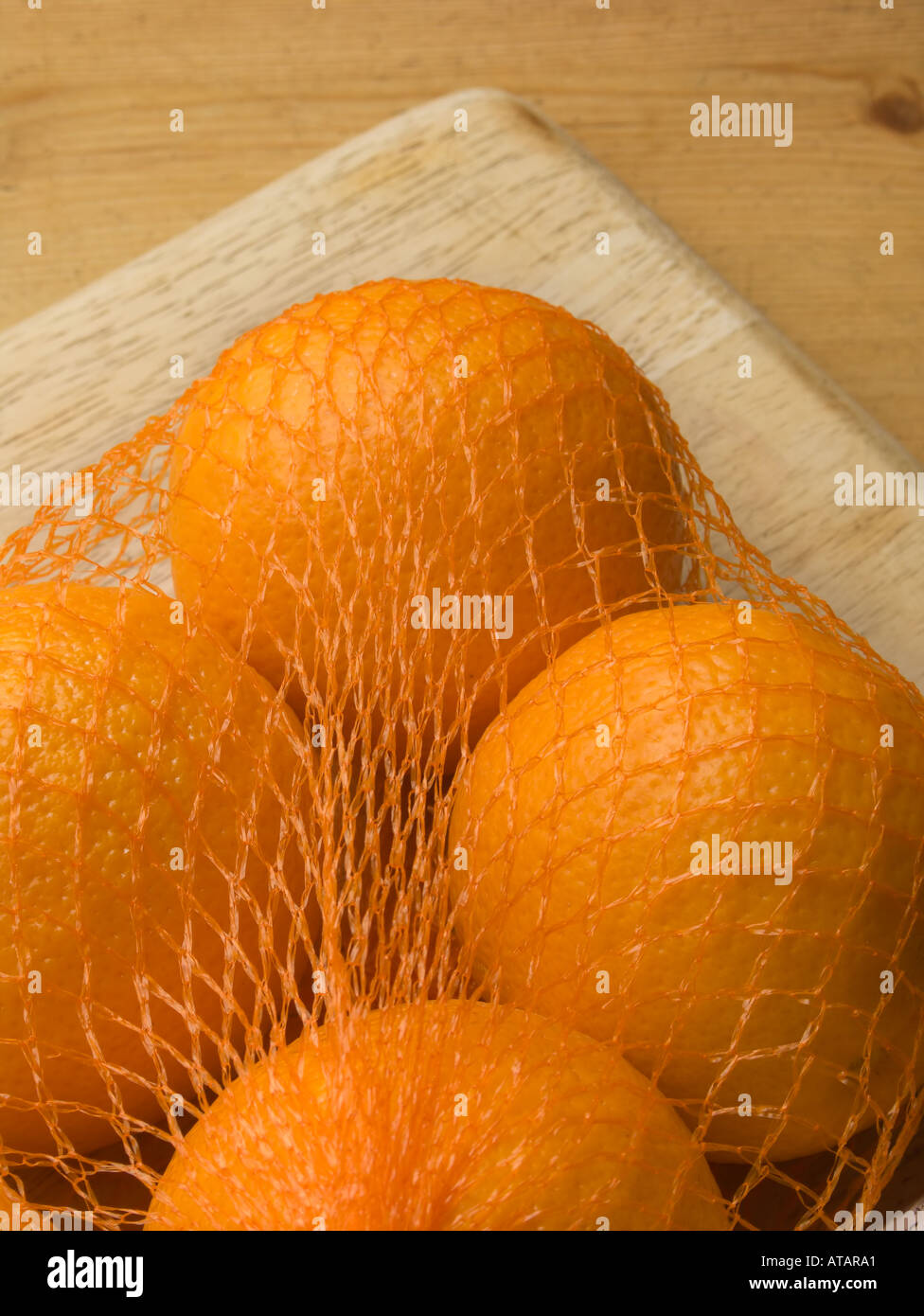 Oranges in net bag on chopping board Stock Photo