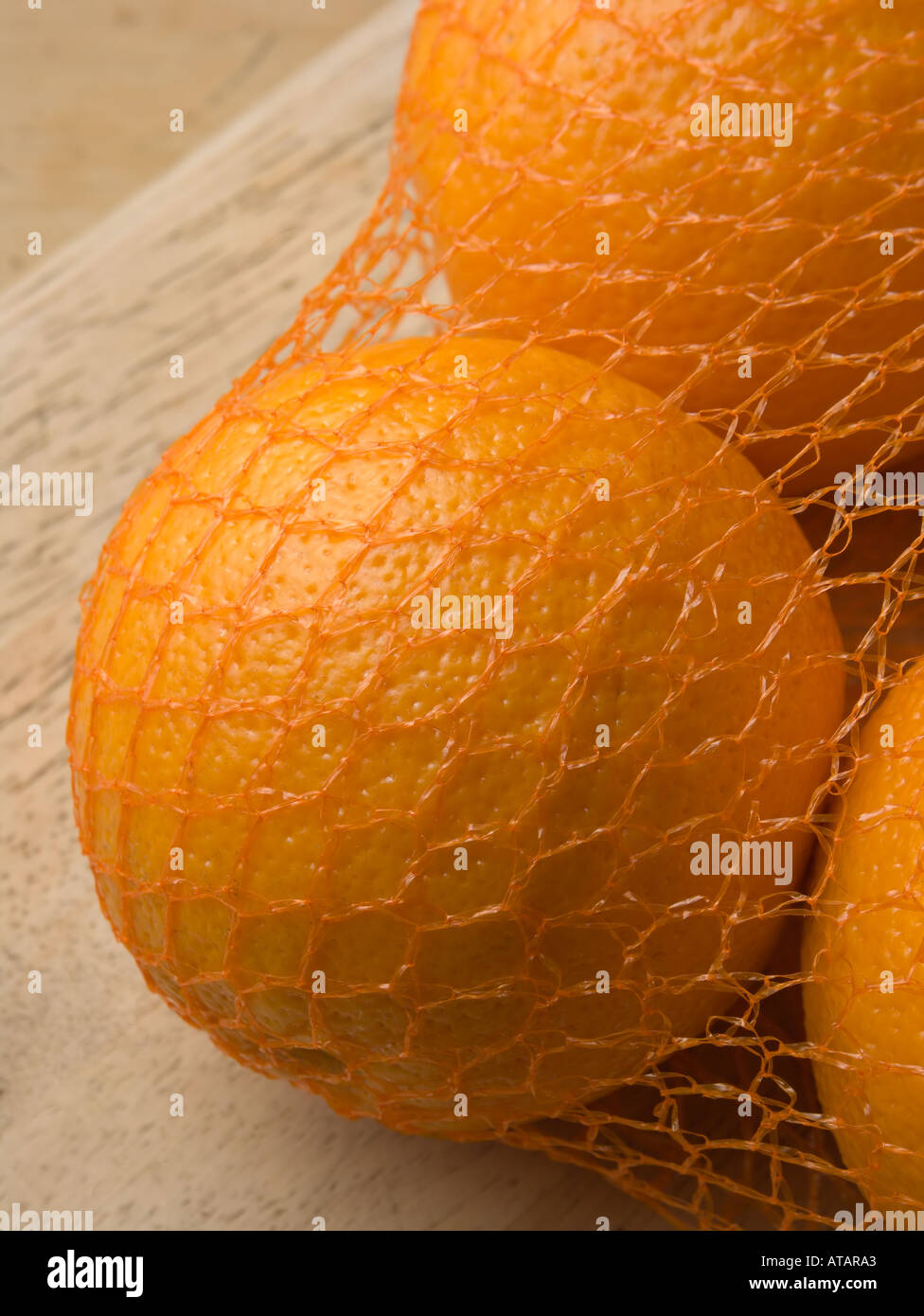 Oranges in net bag on wooden chopping board Stock Photo