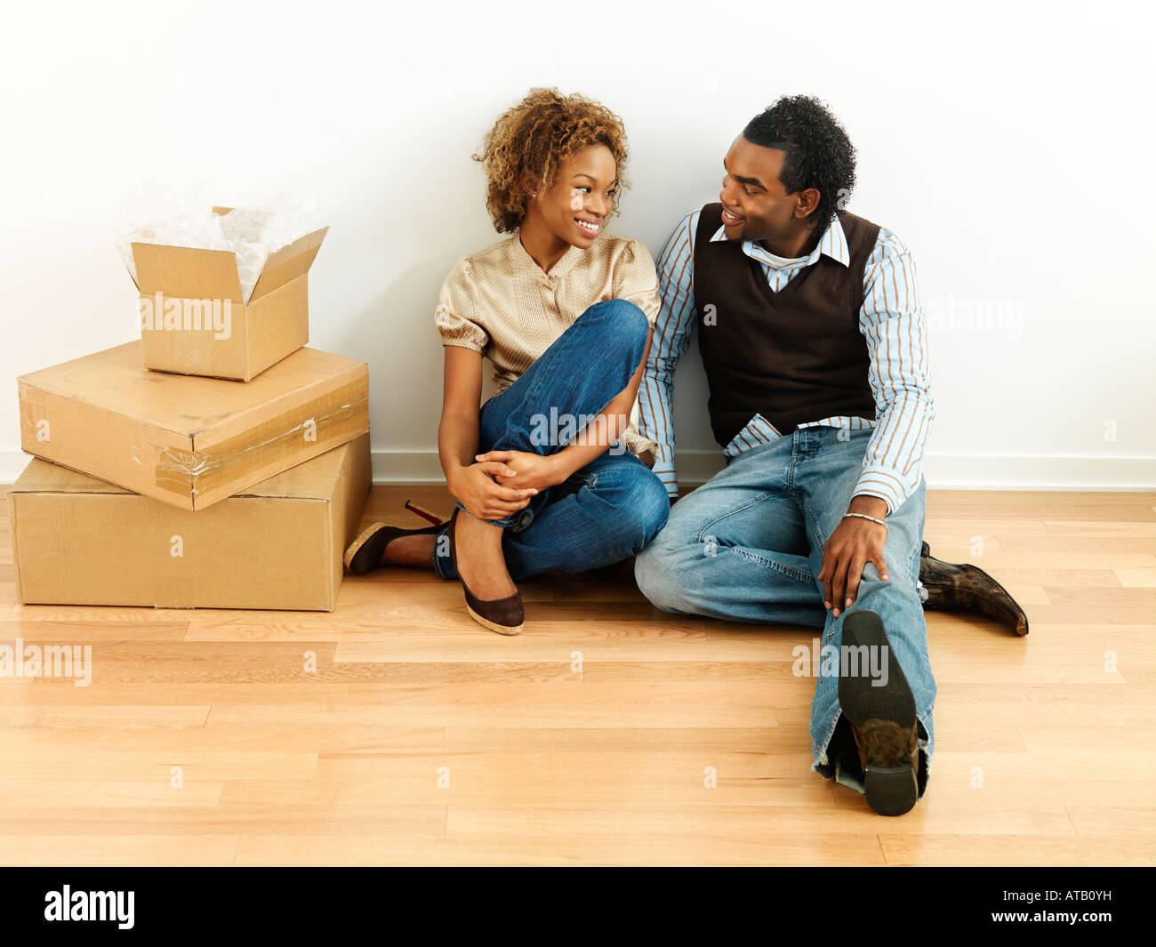 Portrait of smiling happy young couple sitting on floor of home with moving boxes Stock Photo