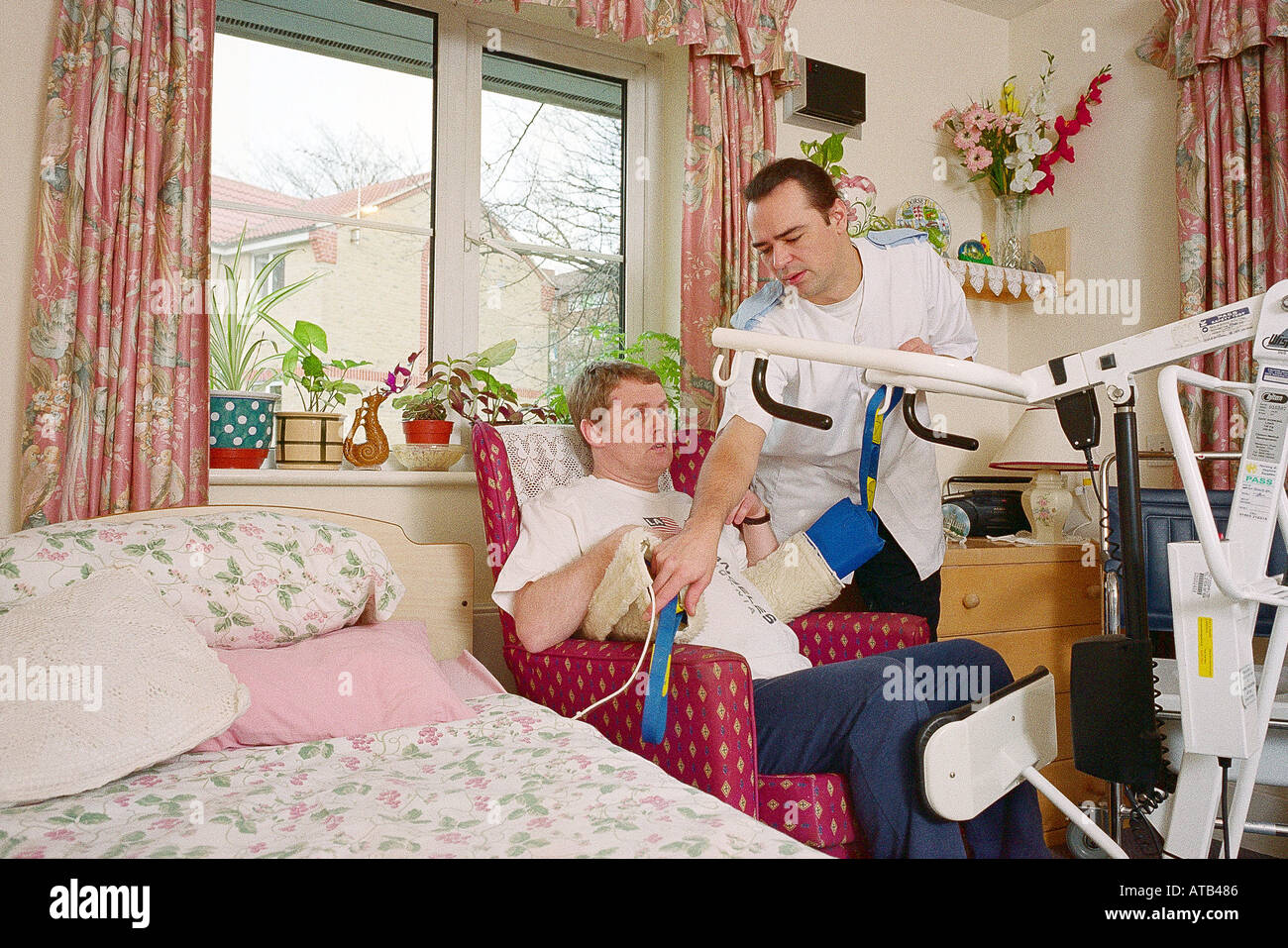 Moving and handling nurse moving patient using mobile hoist Stock Photo